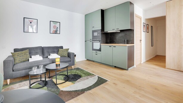 A modern living room with a grey sofa, a small coffee table, and a kitchen with green cabinets and a microwave. - Charming Studio for 2P - Near Parc Monceau (Paris)