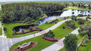 A golf course with a pond, surrounded by lush greenery and a flagpole with an American flag.