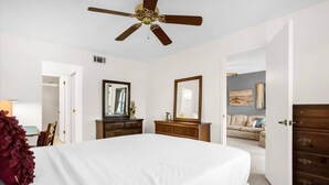 A bedroom with a large bed, two dressers, a ceiling fan, and a door leading to another room. - Upstay Golfer's Retreat w Patio at Ventura Resort (Orlando)