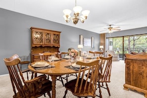 A dining room with a wooden table set for six, surrounded by six wooden chairs. There is a wooden cabinet with glass doors, a chandelier, and a ceiling fan. - Upstay 2BR Golfer's Retreat w Patio Ventura Resort (Orlando)