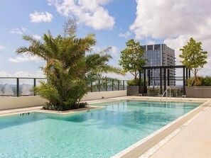A rooftop pool with clear water, surrounded by palm trees and a modern building in the background. - Casiola Residences at The Crosby (Miami)