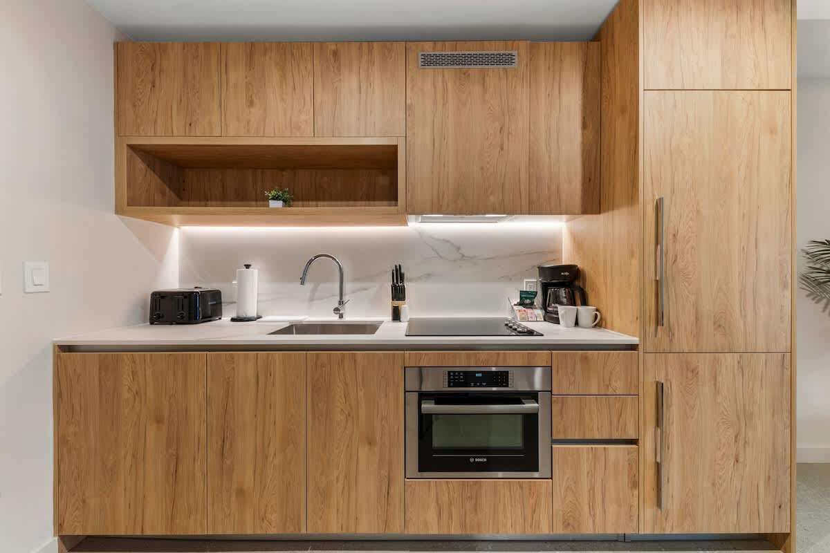 A modern kitchen with wooden cabinets, a built-in oven, and a countertop with a sink and various appliances.