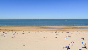 A wide beach with clear skies, a calm sea, and a few boats in the distance.