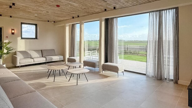 A spacious living room with a large sofa, round coffee tables, and a view of a green landscape through large windows.