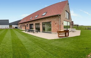 Un bâtiment moderne doté d’un toit en pente, de grandes fenêtres et d’un patio aménagé avec des sièges extérieurs.