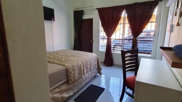 A bedroom with a bed, desk, chair, ceiling fan, and window with curtains. - Zacatecoluca House (Zacatecoluca)