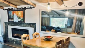 Un coin repas avec une table et des chaises en bois, une cheminée et une grande fenêtre donnant sur un jardin.