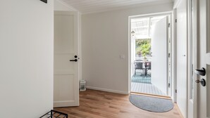 Un couloir doté d’un plancher en bois, de murs blancs et d’une porte donnant sur un espace extérieur aménagé avec une table et des chaises.