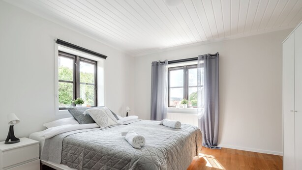 Une chambre à coucher avec un lit, des tables de chevet, une fenêtre avec des rideaux et une vue sur la verdure à l’extérieur.