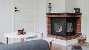 Une pièce avec une porte blanche, une cheminée avec un manteau en briques, une petite table sur laquelle se trouve une tasse blanche et un panier en osier.
