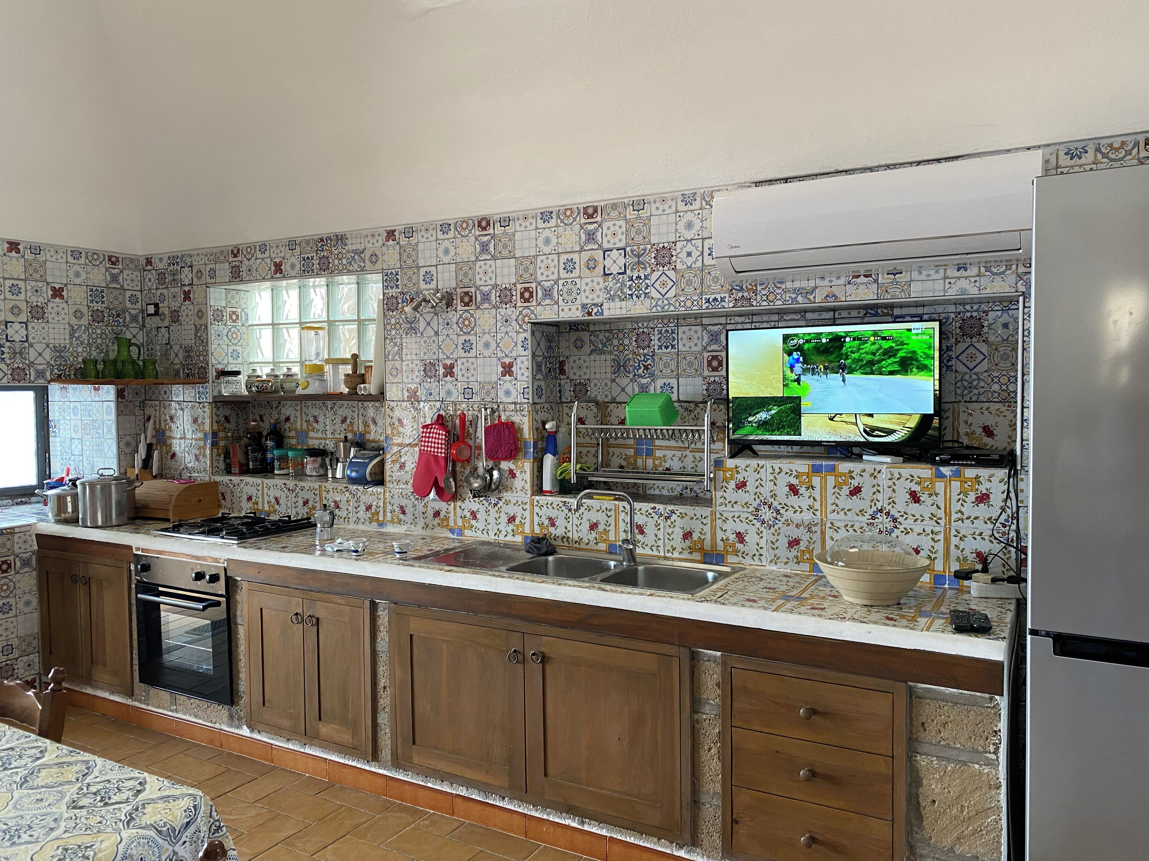 Una cocina con gabinetes de madera, una estufa, un lavamanos y un televisor montado en la pared.