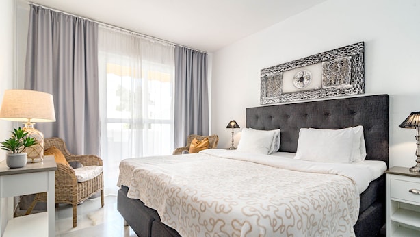 Een moderne hotelkamer met een groot bed, een nachtkastje, een stoel, een lamp en een raam met gordijnen.