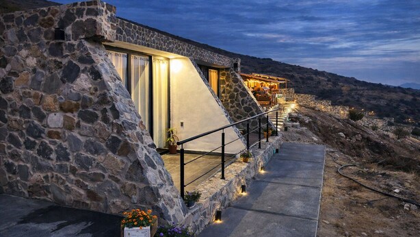 A stone building with a sloped roof, a staircase leading to a lit upper level, and a pathway with potted plants. - Complejo Turístico Mixcóatl  (San Martín de las Pirámides)