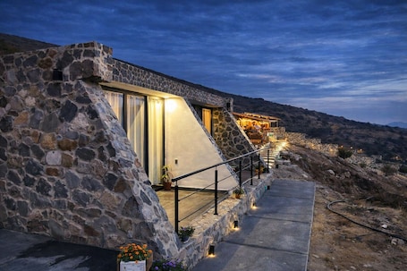 A stone building with a sloped roof, a staircase leading to a lit upper level, and a pathway with potted plants.. Complejo Turístico Mixcóatl