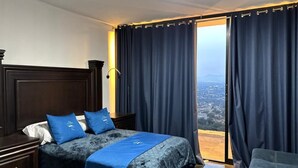A hotel room with a bed, a nightstand, a chair, and a view of a cityscape through the window. - Complejo Turístico Mixcóatl  (San Martín de las Pirámides)