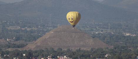 A hot air balloon with a smiling face, flying over a town with buildings and hills in the background.