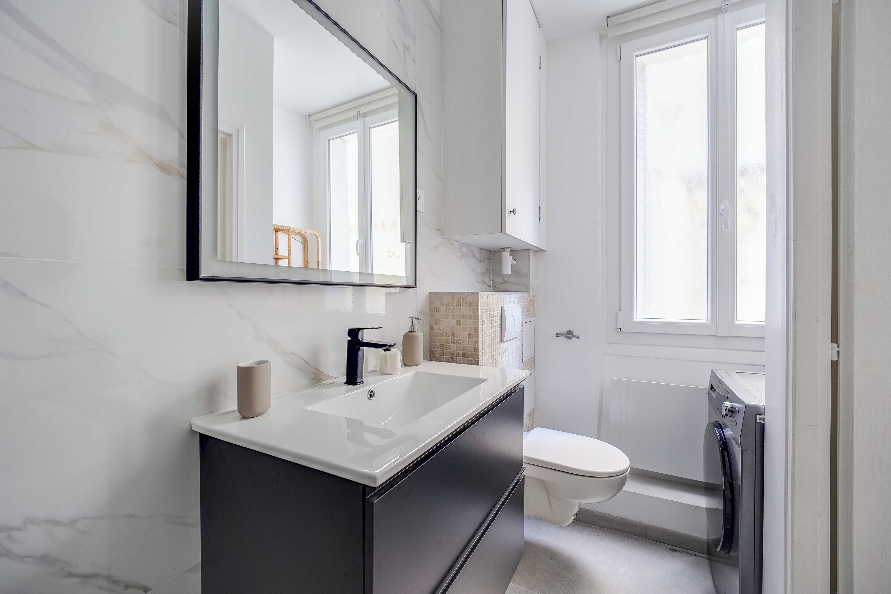 A modern bathroom with a large mirror, a sink, a toilet, and a shower.