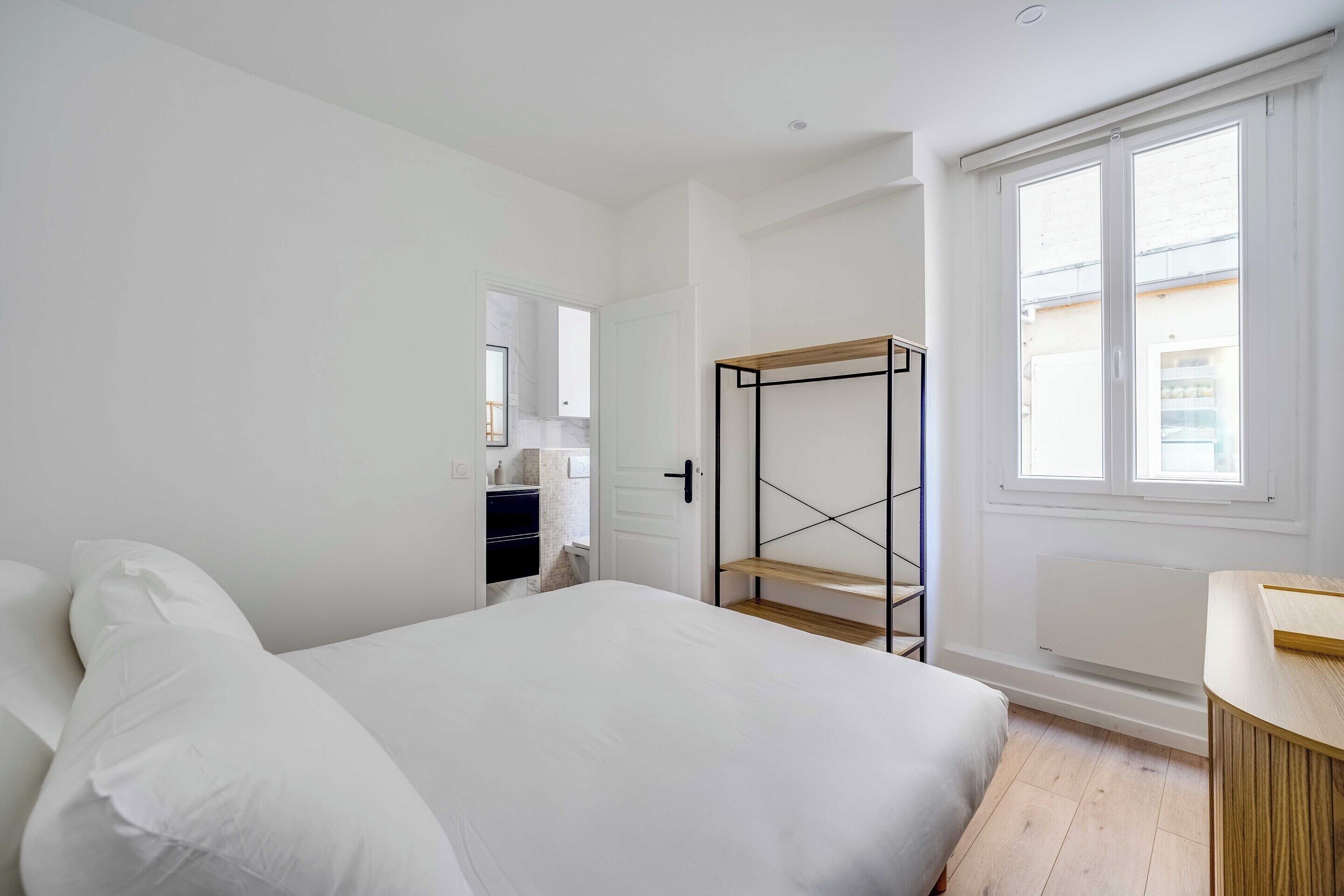A bedroom with a bed, a wooden shelf, a radiator, and a window.