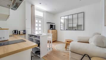 Eine moderne Küche mit Mikrowelle, Wasserkocher und Kaffeemaschine; ein Essbereich mit Tisch und Stühlen; ein Sofa; und ein großer Spiegel.