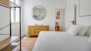 Una camera da letto con un letto, una cassettiera in legno, uno specchio rotondo e una finestra.
