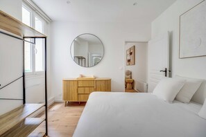 Un dormitorio con una cama, un aparador de madera, un espejo redondo y una ventana.