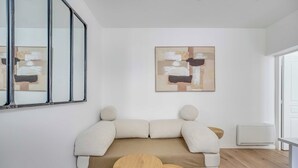 Un soggiorno moderno con un divano, due tavolini in legno, un grande quadro astratto e una finestra.