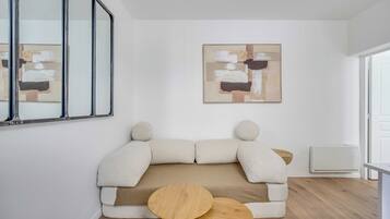 Ein modernes Wohnzimmer mit einer Couch, zwei kleinen Holztischen, einem großen abstrakten Gemälde und einem Fenster.