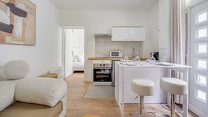 Una cucina moderna con mobili bianchi, un forno a microonde integrato e un piccolo forno. C'è un'area pranzo con un tavolo bianco e due sgabelli da bar.