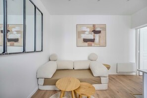 A minimalist living room with a sofa, two small wooden tables, and abstract art on the wall. - Modern Apartment 1br/4p - Levallois (Levallois-Perret)