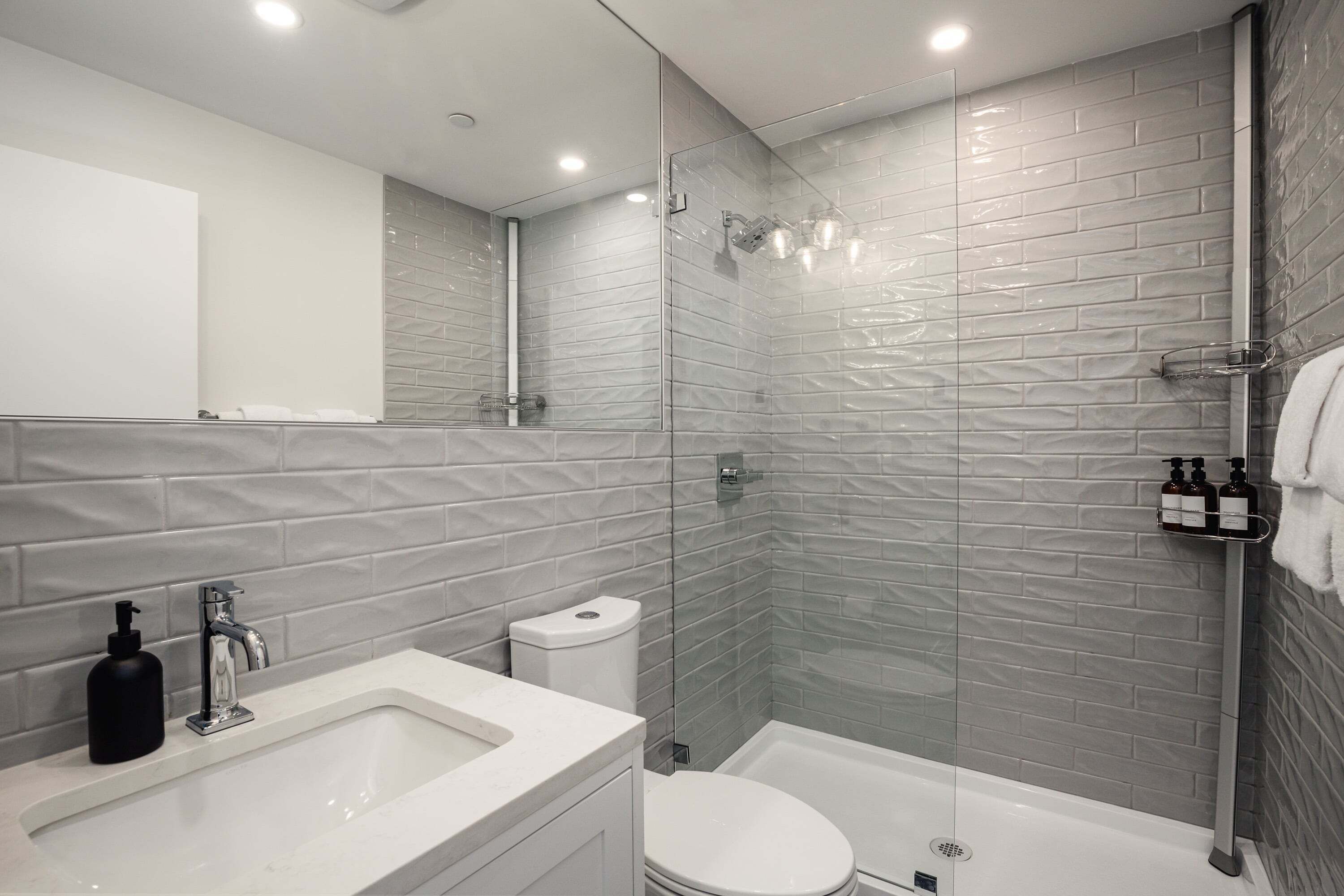 Een moderne badkamer met een glazen douchecabine, een wit wastafelmeubel en een toilet.