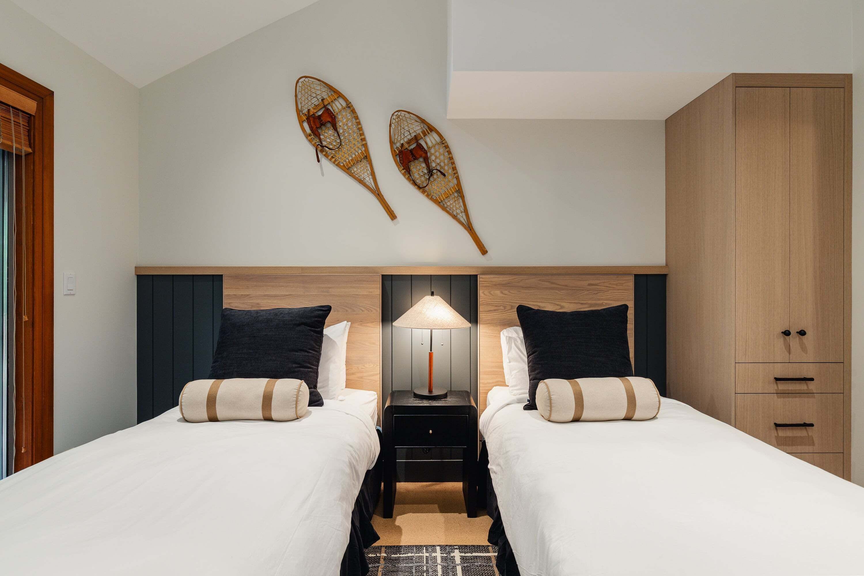 A hotel room with two beds, a nightstand with a lamp, and a wardrobe.