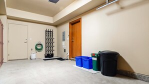 A hallway with a door, a coat rack, a gas cylinder, and trash bins. - Harmony Chalet at Montebello (Whistler)