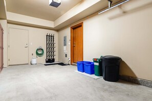 A hallway with a door, a coat rack, a gas cylinder, and trash bins. - Harmony Chalet at Montebello (Whistler)