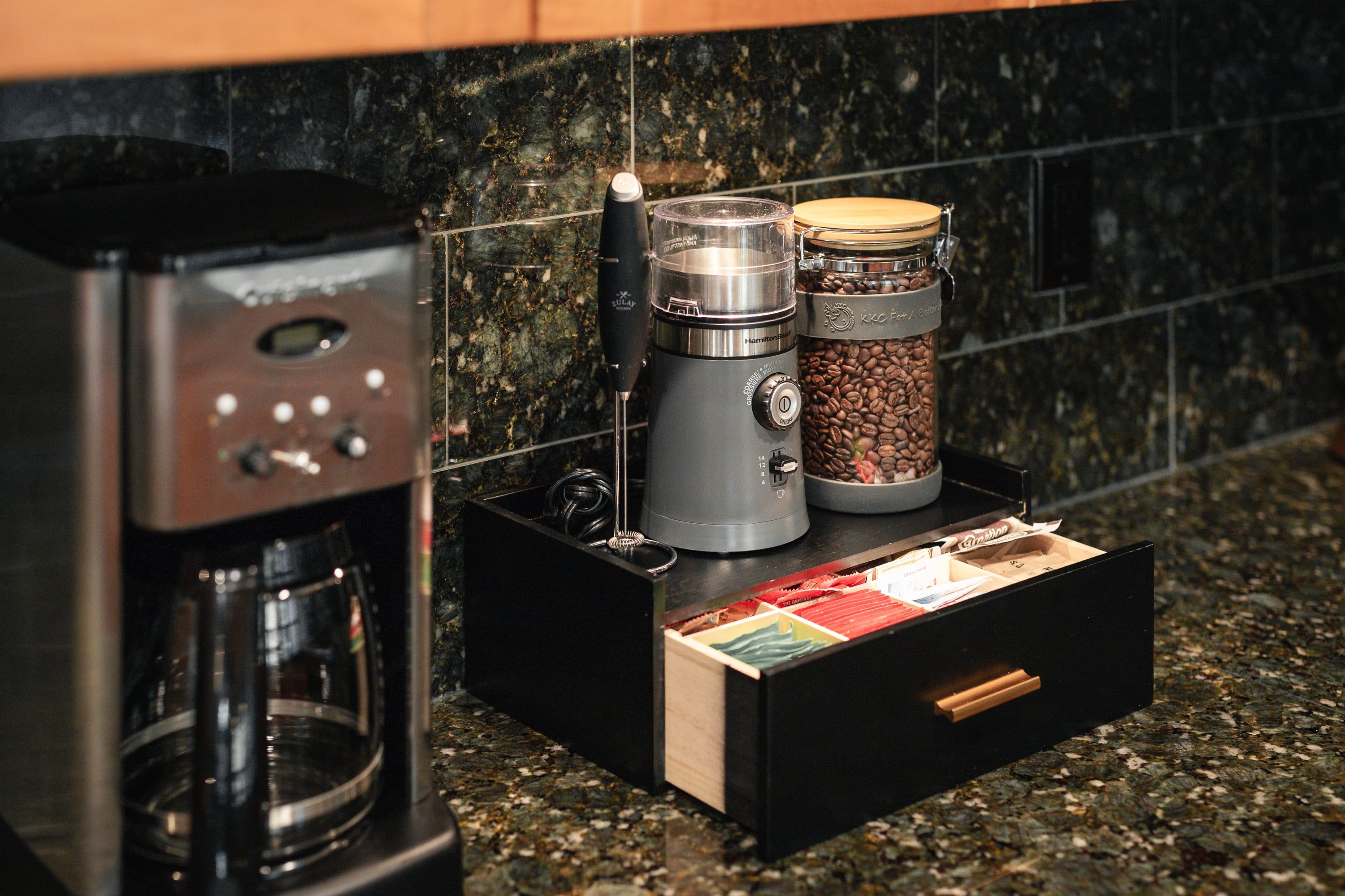 Un plan de travail de cuisine avec une machine à café, un moulin à café et un récipient rempli de grains de café.