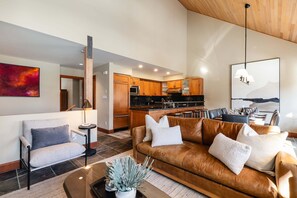 Ein modernes Wohnzimmer mit Ledersofa, Couchtisch mit Pflanzen, Essbereich mit Tisch und Stühlen sowie Küche mit Holdekor-Schränken und schwarzer Arbeitsplatte.