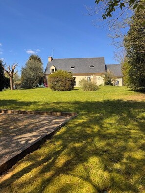 Une maison avec un toit en pente, un petit jardin et une zone pavée au premier plan.