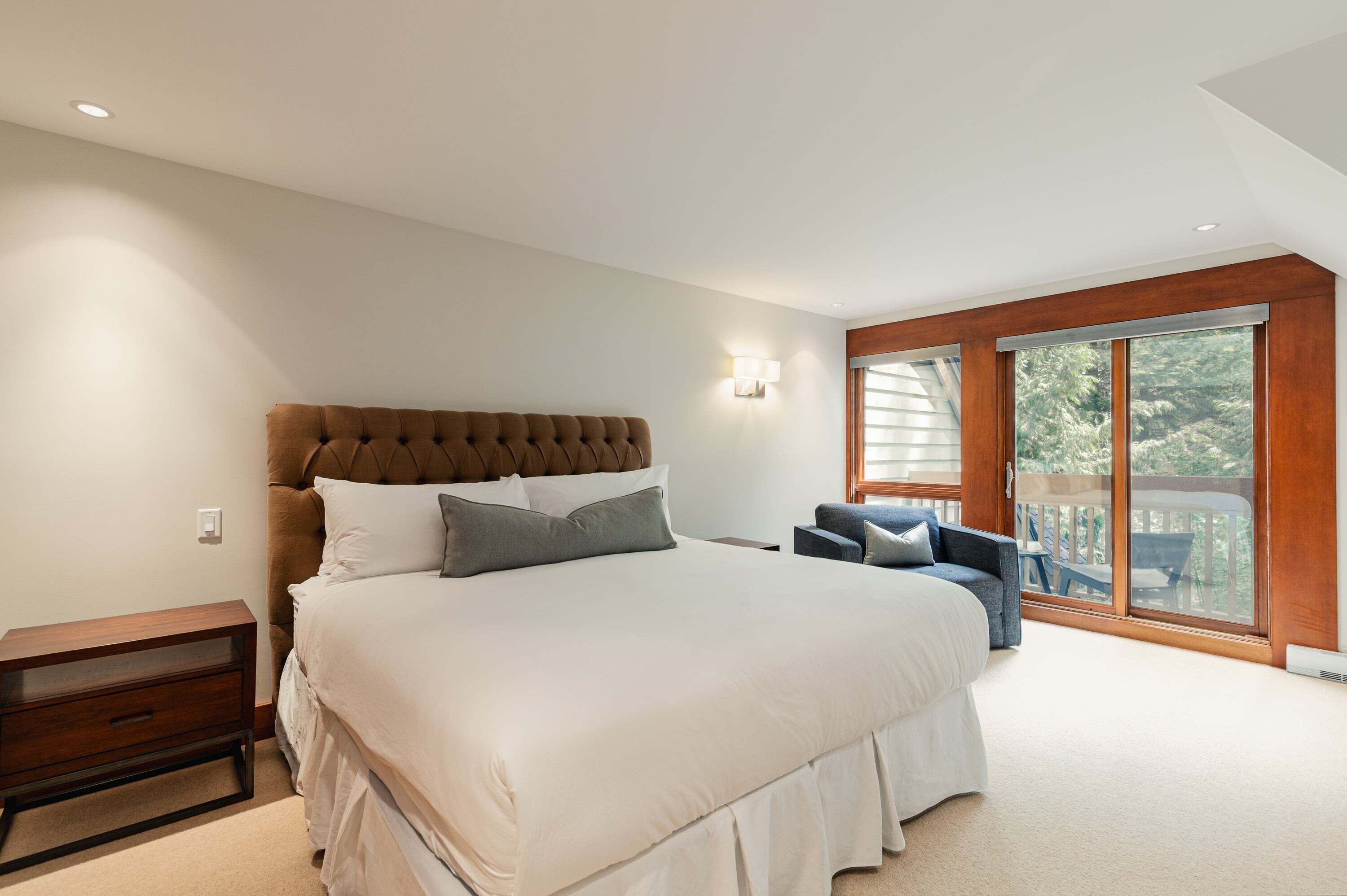 A bedroom with a large bed, a nightstand, a chair, and a sliding glass door leading to an outdoor area.