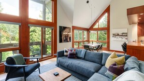 A spacious living area with a large sofa, a coffee table, and a dining area with a table and chairs. - Northlight Retreat at Alpine Greens (Whistler)