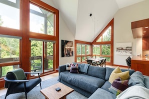 A spacious living area with a large sofa, a coffee table, and a dining area with a table and chairs. - Northlight Retreat at Alpine Greens (Whistler)