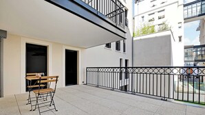 Un balcon avec une table et des chaises, une rambarde en métal noir et un bâtiment en arrière-plan.