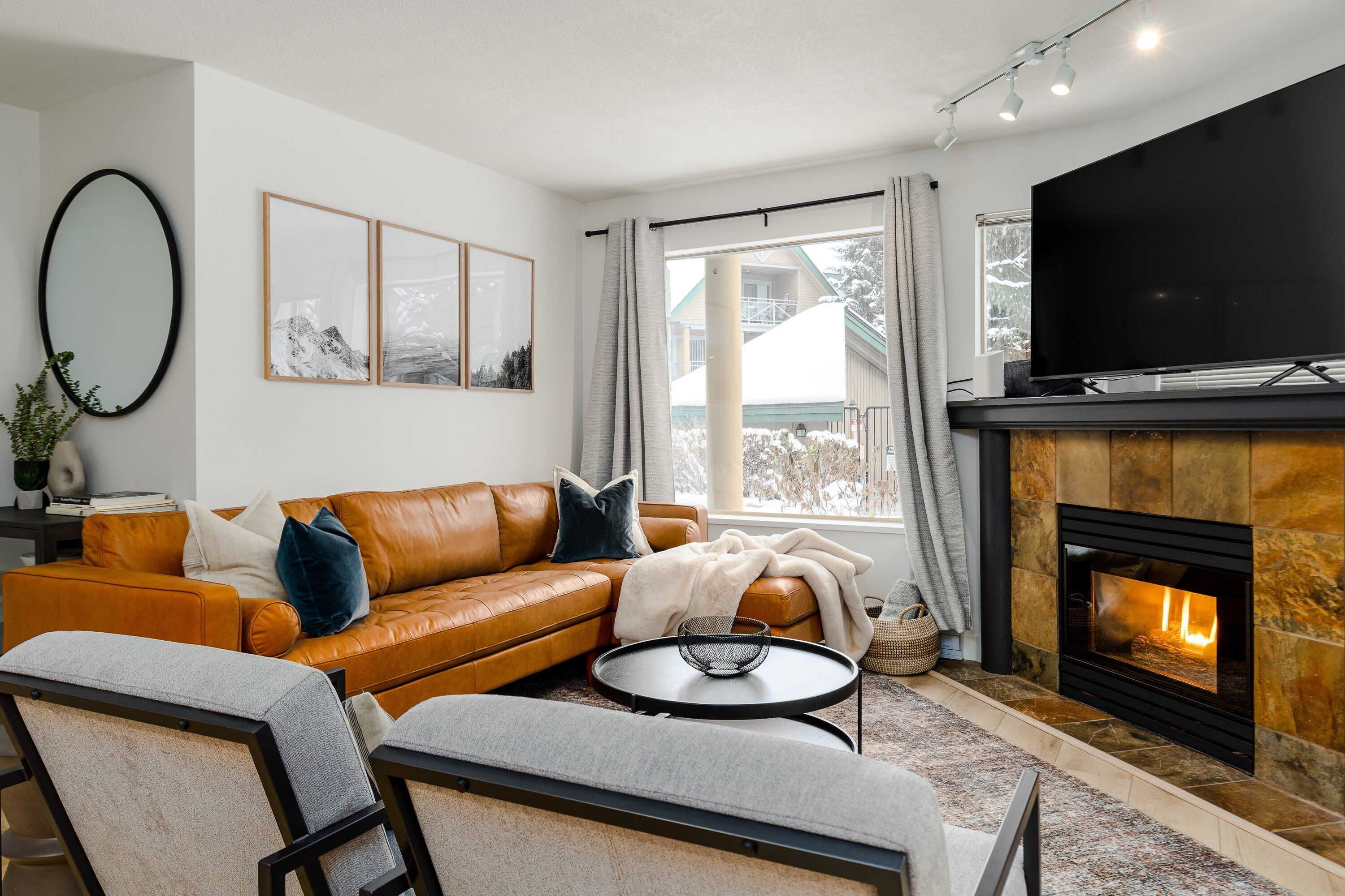 Ein modernes Wohnzimmer mit Ledersofa, Flachbildfernseher, Kamin und großem Fenster mit Vorhängen.