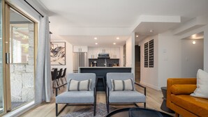 A modern kitchen with white cabinets and stainless steel appliances, a dining area with a table and chairs, and a living area with a sofa and a coffee table. - The Altitude at Valhalla (Whistler)