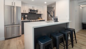 A modern kitchen with stainless steel appliances, a central island with stools, and a microwave above the stove. - The Altitude at Valhalla (Whistler)