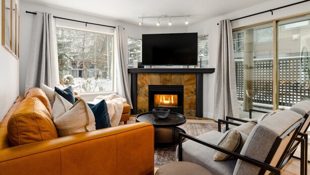 A modern living room with a fireplace, a sofa, a chair, and a television. - The Altitude at Valhalla (Whistler)