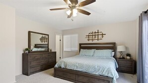 Un dormitorio con cama, cómoda, espejo, ventilador de techo e iluminación empotrada en la pared.