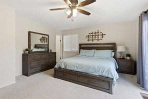 Ein Schlafzimmer mit Bett, Kommode, Spiegel, Deckenventilator und einer Wandleuchte.