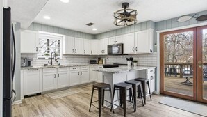 Una cocina con gabinetes blancos, una isla central con taburetes, un microondas y un ventilador de techo.