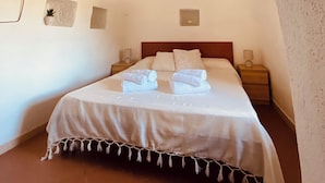 Une chambre à coucher comprenant un lit, une table de chevet, une lampe fixée au mur et une poutre au plafond.