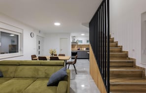 A modern interior with a green sofa, dining table, kitchen, and wooden staircase.