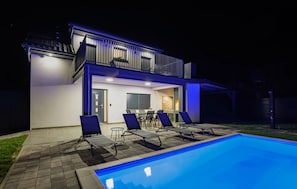 Une maison moderne à deux étages, dotée d’une piscine, d’un espace extérieur aménagé et d’un patio couvert.